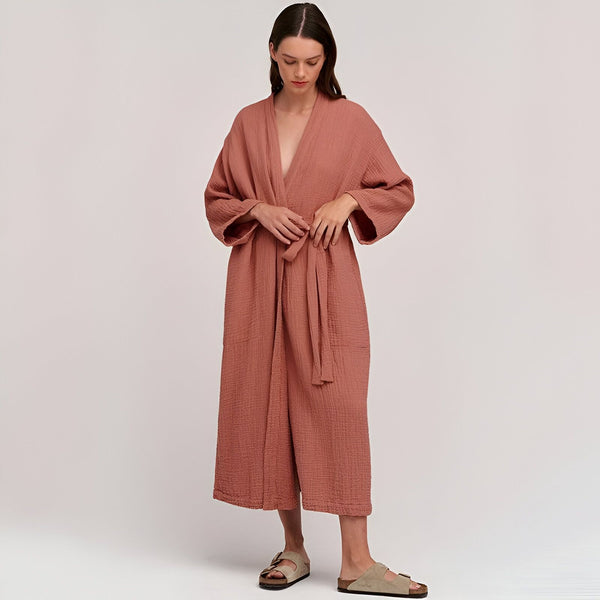 Femme portant un kimono long rose en coton, noué à la taille. Peignoir style japonais, vêtement d'intérieur confortable et élégant. Boutique de kimonos en ligne.