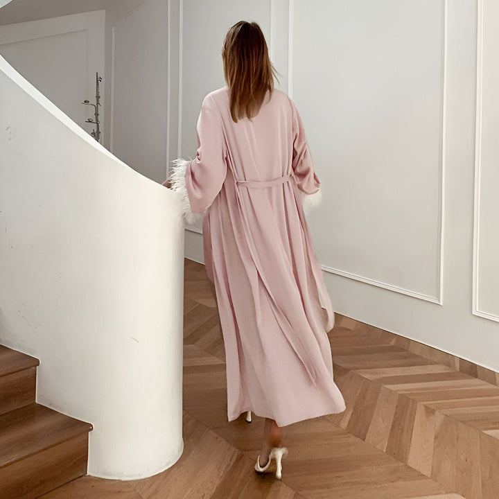Femme portant un kimono rose avec des plumes, vue de dos. Vêtements de détente de luxe. Kimonos élégants disponibles à l'achat.