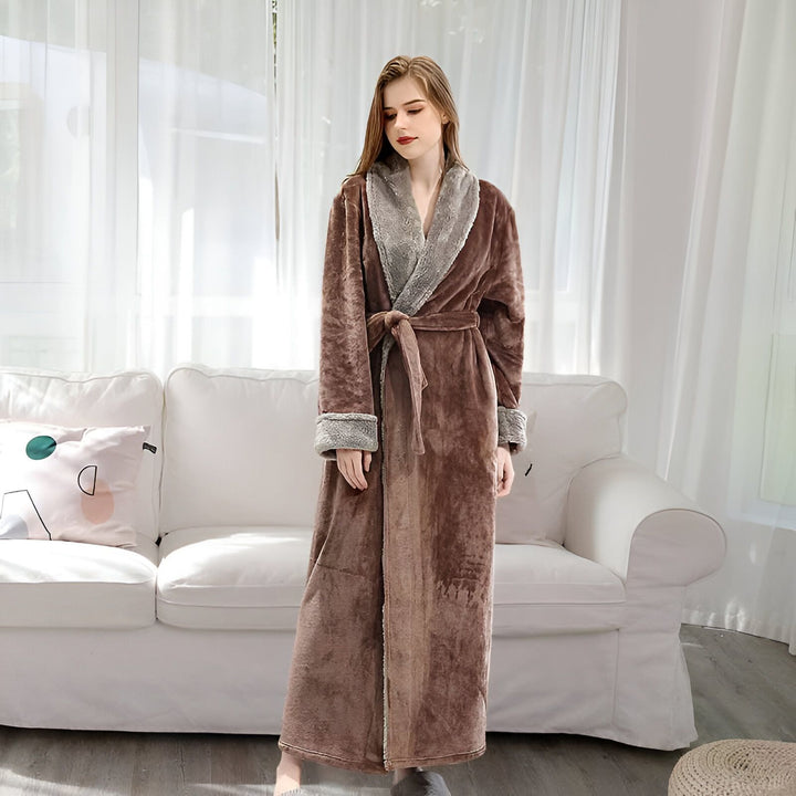 Femme portant un long peignoir marron en velours avec col en fausse fourrure grise. Peignoir kimono avec ceinture, idéal pour la détente à la maison. Confort et élégance garantis.