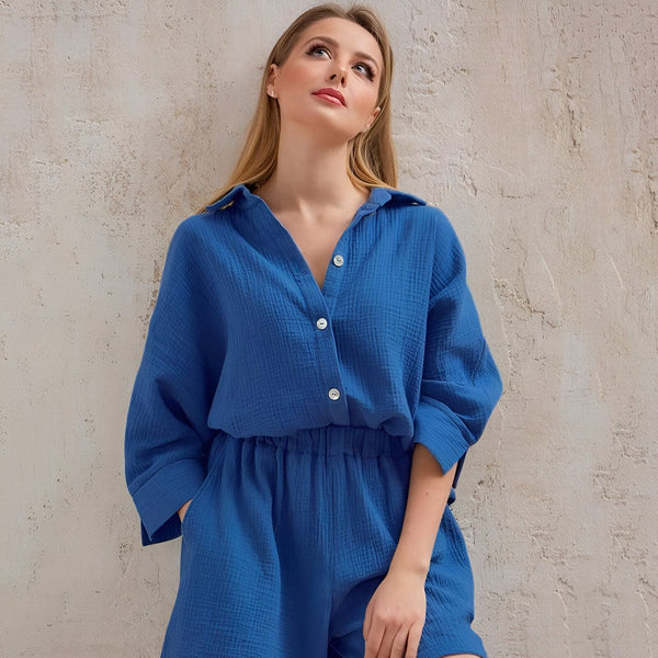 Femme portant un ensemble bleu décontracté, chemise et short assortis, devant un mur texturé. Kimono d'intérieur confortable.