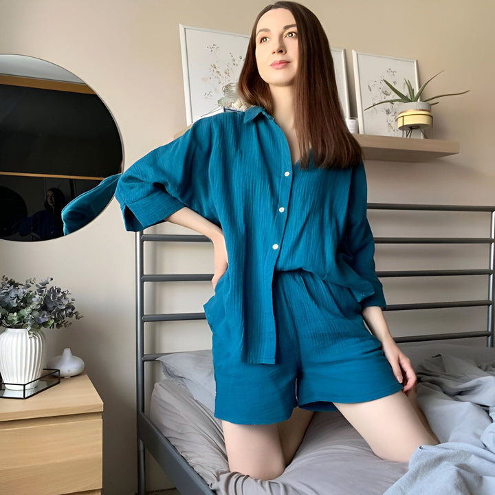 Femme en ensemble kimono bleu turquoise, chemise et short assortis, assise sur un lit. Vente de kimonos pour femmes, style décontracté.