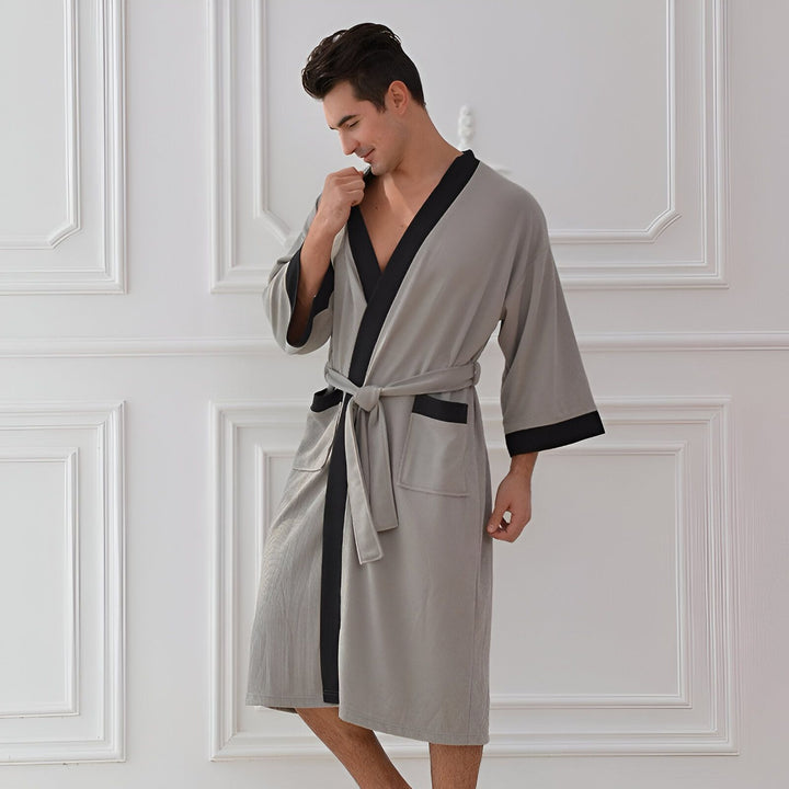 Homme portant un kimono gris avec bordure noire et ceinture. Vêtements de détente élégants.
