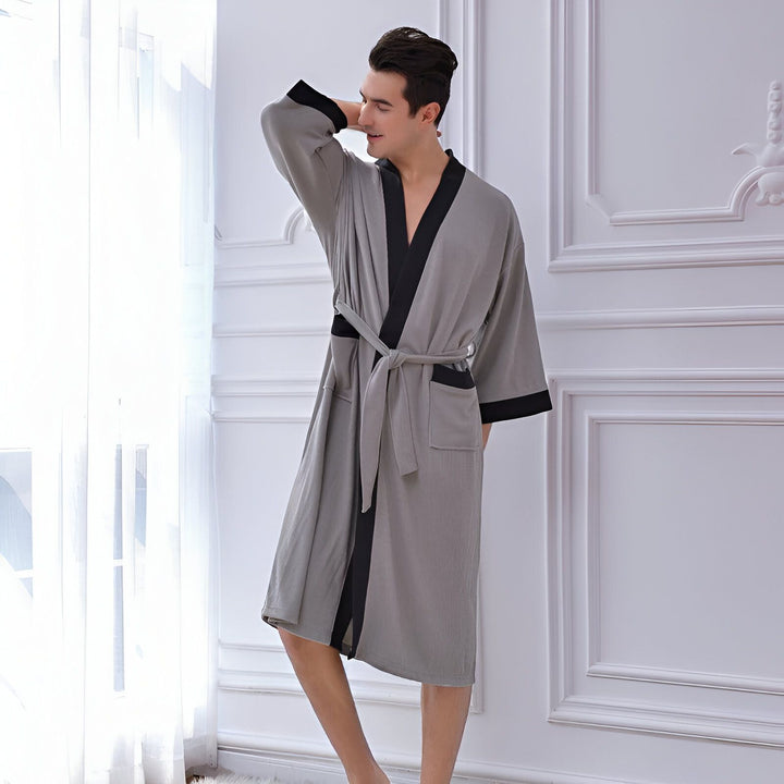 Homme portant un kimono gris avec bordure noire et ceinture. Vêtements de détente confortables pour la maison. Découvrez notre collection de kimonos de qualité.