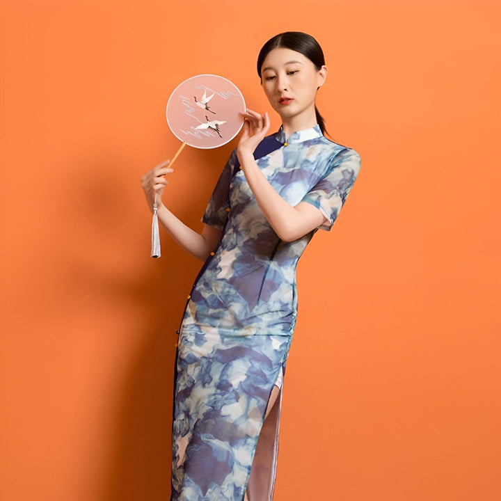 Femme asiatique en kimono bleu à motifs, tenant un éventail rond avec des grues. Vente de kimonos traditionnels et modernes. Découvrez notre collection de kimonos uniques.