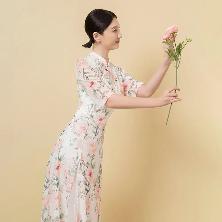 Femme en kimono floral blanc et rose, tenant une fleur. Élégance et tradition asiatique. Découvrez nos kimonos uniques.