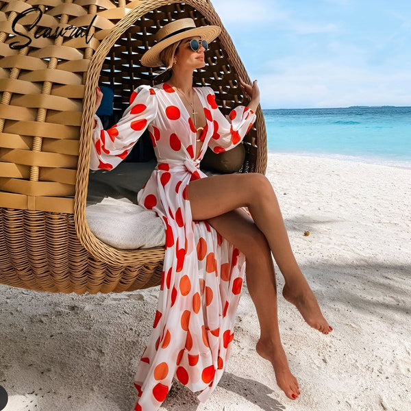 Femme portant un kimono à pois rouges sur la plage, assise dans un fauteuil suspendu en osier. Look estival décontracté avec chapeau et lunettes de soleil. Vente de kimonos pour la plage et les vacances.