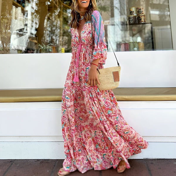 Femme souriante en longue robe kimono fleurie rose et blanche, avec un sac bandoulière en paille. Parfait pour un look bohème chic!