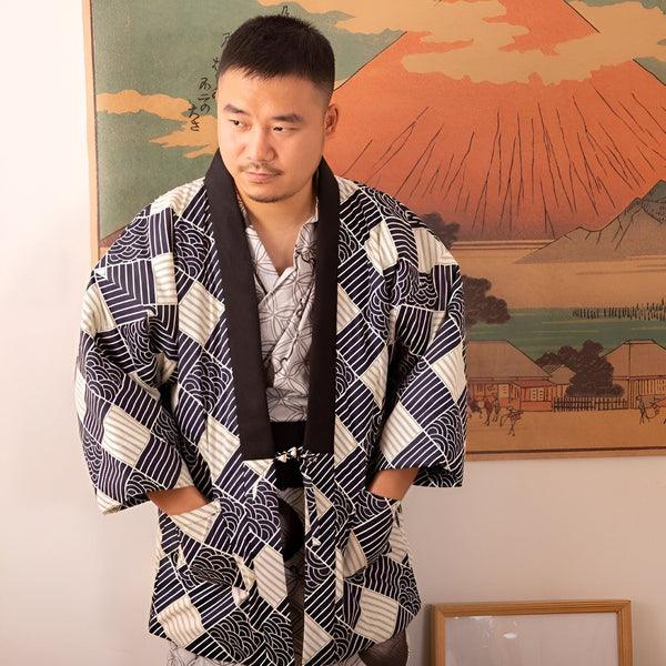 Homme portant un kimono traditionnel japonais bleu marine et blanc à motifs géométriques, devant une estampe du Mont Fuji. Kimonos à vendre.