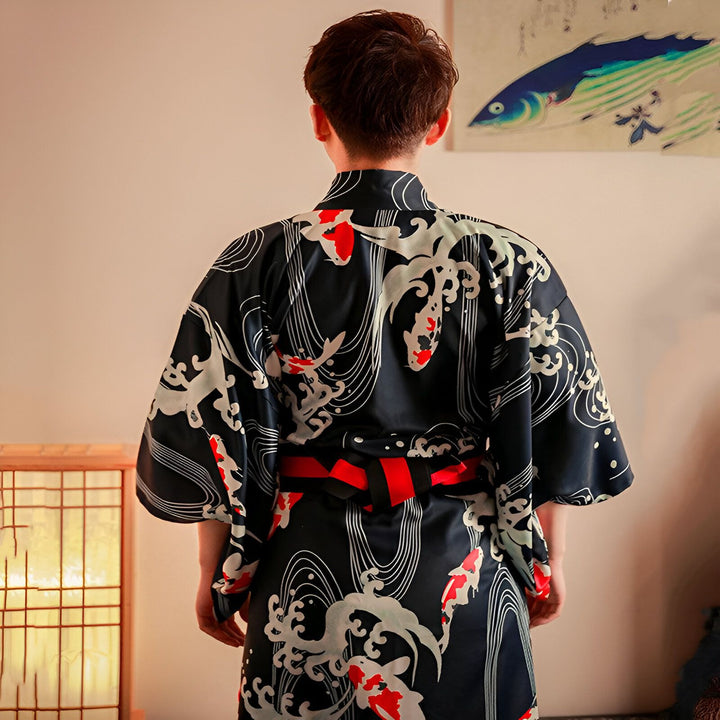 Homme portant un kimono noir à motifs de carpes koï rouges et vagues blanches. Vêtement traditionnel japonais avec ceinture obi rouge et noire. Vue de dos.