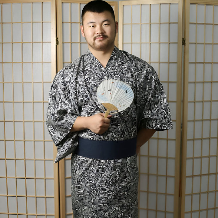 Homme portant un kimono japonais à motif de vagues avec une ceinture obi bleue, tenant un éventail. Vêtements traditionnels, mode japonaise.